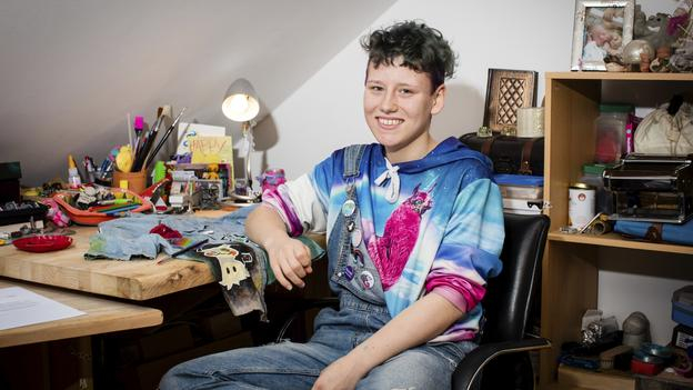 René sitzt an seinem Schreibtisch und lächelt in die Kamera.