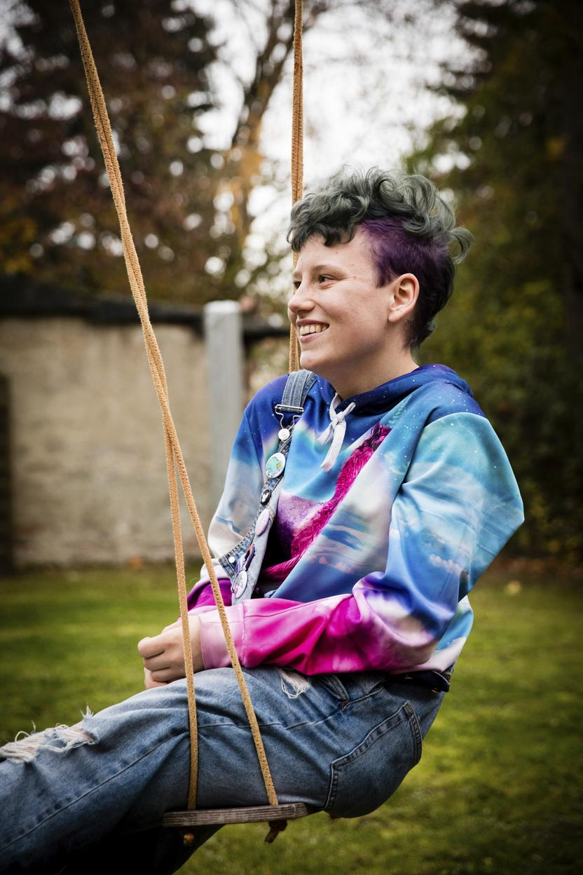 René sitzt in einem bunten Pullover auf einer Schaukel.