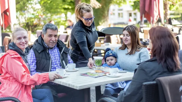 Vier Menschen sitzen draußen in einem Cafe im Sonnenschein.