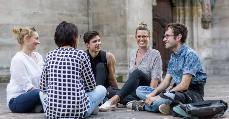 Eine Gruppe von Menschen sitzt auf dem Boden vor einer Kirche