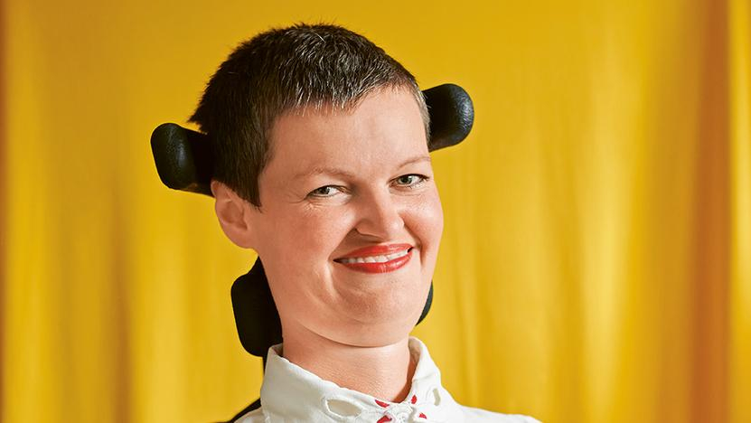 Eine Frau mit kurzen Haaren im Rollstuhl lächelt