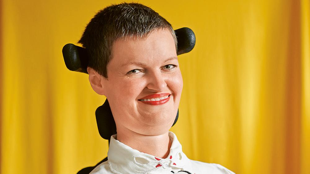 Eine Frau mit kurzen Haaren im Rollstuhl lächelt