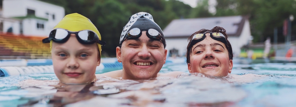 Zwei Jungen und ein Mädchen schwimmen im Schwimmbecken.