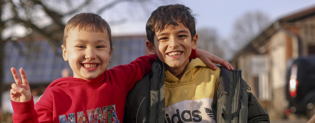 Zwei Jungs haben sich gegenseitig die Arme um die Schultern gelegt. Sie lachen in die Kamera.
