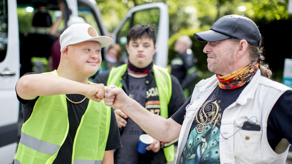 Ein Mann mit Downsyndrom begrüßt einen anderen Mann freundschaftlich mit einem Faust-Gruß. Beide gehören zu einem Motorradclub.
