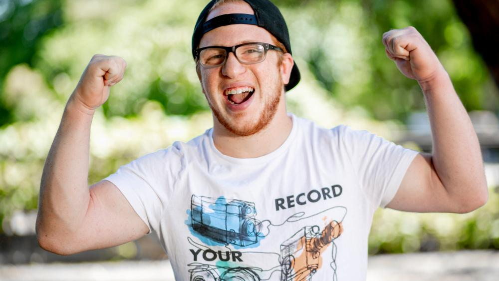 Ein Mann mit Kappe und Brille streckt als Zeichen der Stärke seine Arme gebeugt nach oben.