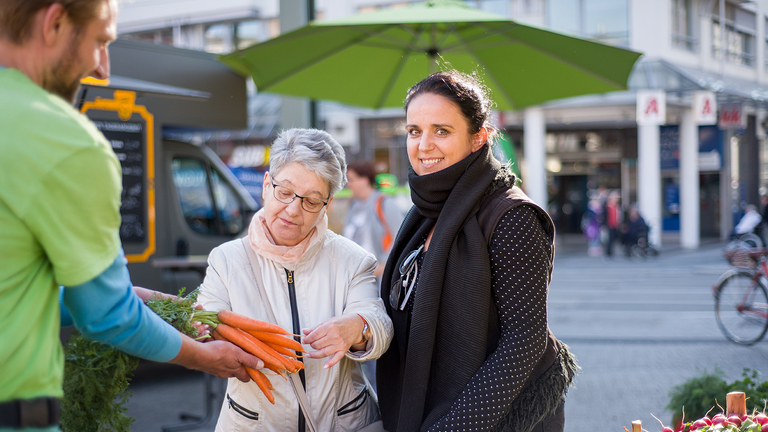 Eine Frau begutachtet die von einem Obstverkäufer präsentierten Möhren