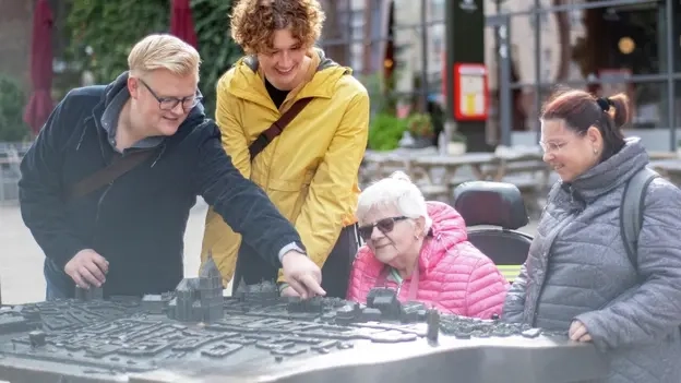 Vier Personen, eine sitzt im Rollstuhl, schauen sich eine Stadtkarte an, die man fühlen kann.