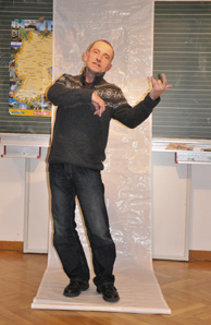 Mann steht vor einer Tafel und macht Bewegung eines Geigenspielers.