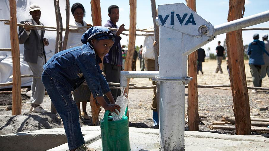 Ein kleines dunkelhäutiges Mädchen zapft Wasser.