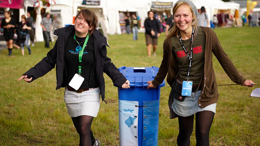 Zwei Mädels sind mit einer Tonne unterwegs. Sie sammeln ehrenamtlich Pfandbecher auf einem Festival.