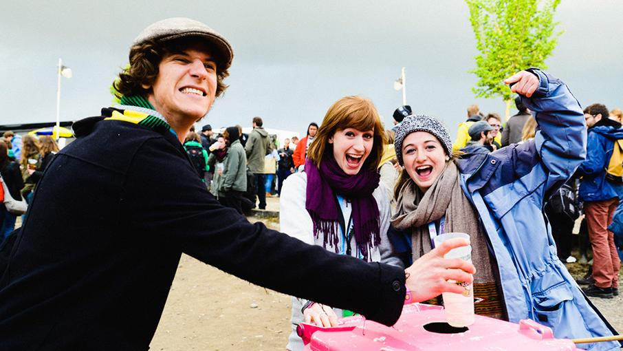 Festivalaktion von Viva con Agua: Ein Typ steckt Plastikbecher in eine Sammeltonne. Hinter ihm jubilieren 2 Mädels.