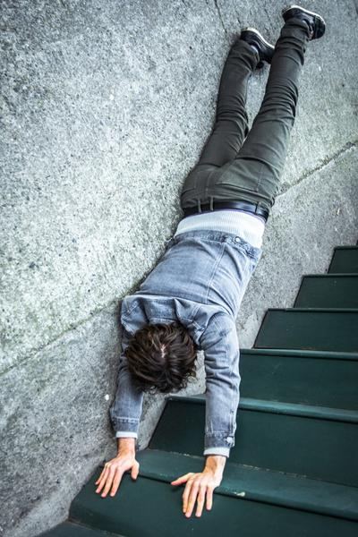 Ein junger Mann macht einen Handstand auf einer Treppenstufe. Die rechte Körperhälfte berührt die Wand.