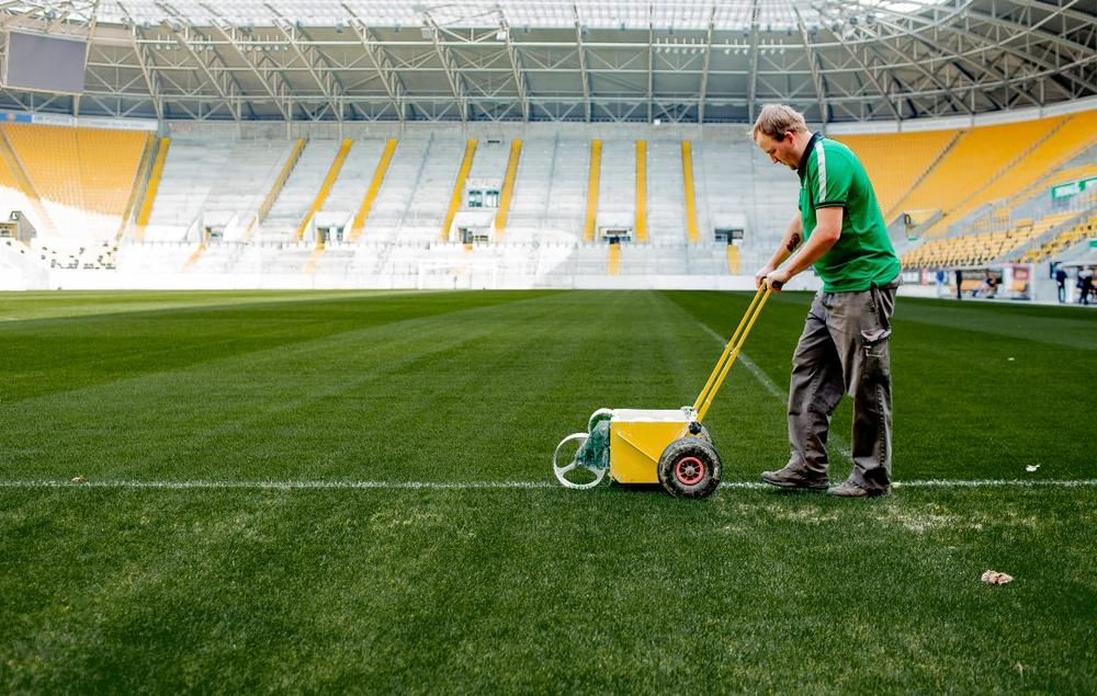 Ein Mann pflegt den Rasen in einem Fußballstadion.