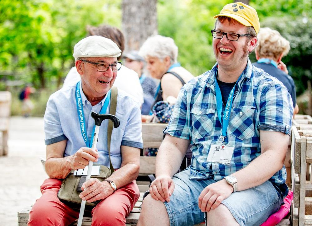 Ein junger und ein alter Mann sitzen auf einer Bank und lachen gemeinsam.
