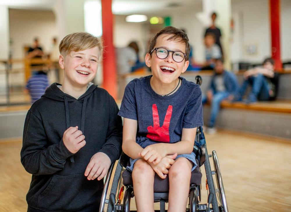 Zwei Jungen, einer davon im Rollstuhl, lachen gemeinsam.