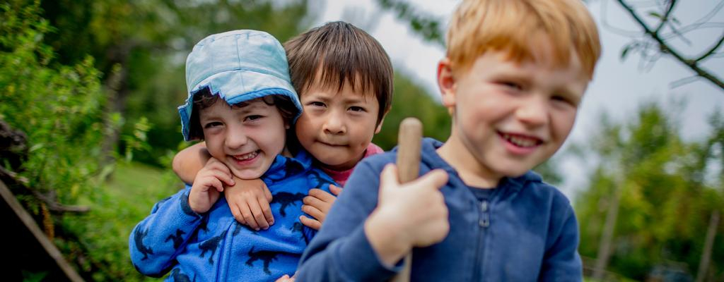 Drei Kinder in der Natur lachen in die Kamera.