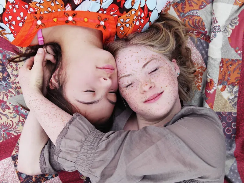 Blick von oben: zwei Mädchen liegen auf einer Decke  mit ihren Köpfen dicht beieinander. 