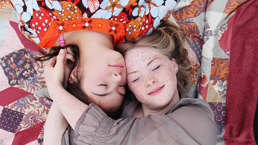 Blick von oben: zwei Mädchen liegen auf einer Decke  mit ihren Köpfen dicht beieinander. 