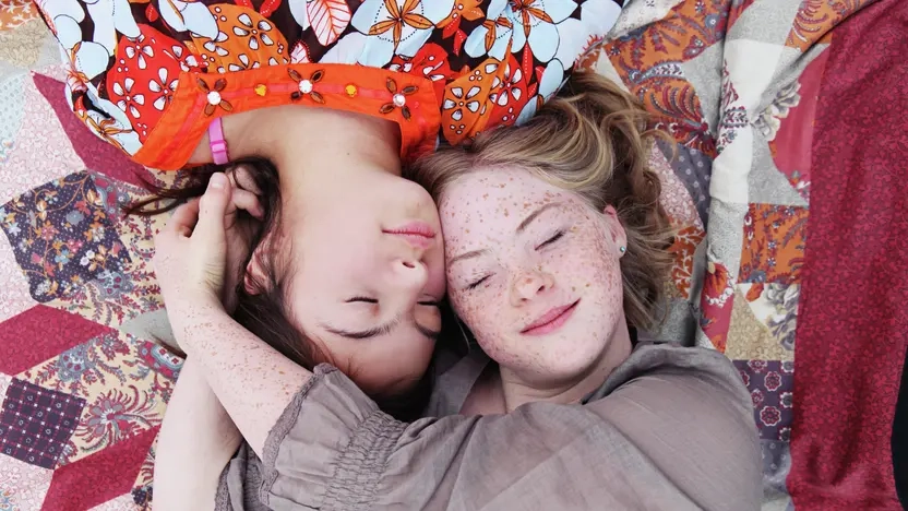 Blick von oben: zwei Mädchen liegen auf einer Decke  mit ihren Köpfen dicht beieinander. 