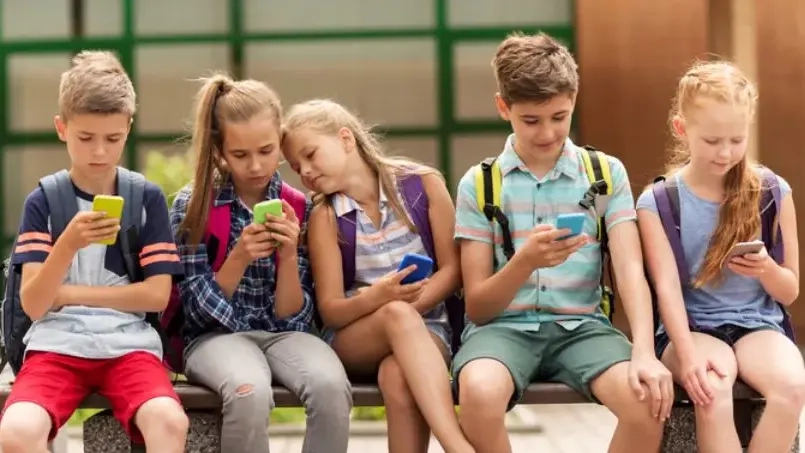 Mehrere Kinder sitzen auf einer Bank. Alle haben ein Handy in der Hand und schauen darauf.