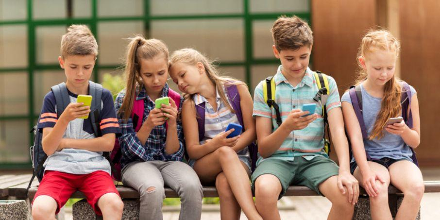 Mehrere Kinder sitzen auf einer Bank. Alle haben ein Handy in der Hand und schauen darauf.