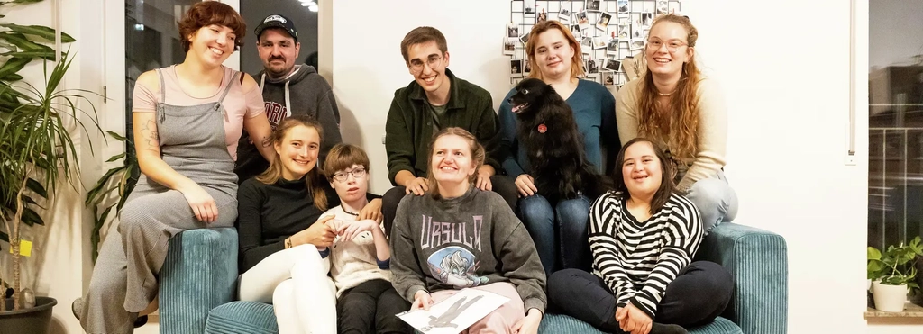 Eine Gruppe von Menschen mit uns ohne Behinderung sitzt gemeinsam auf einem Sofa