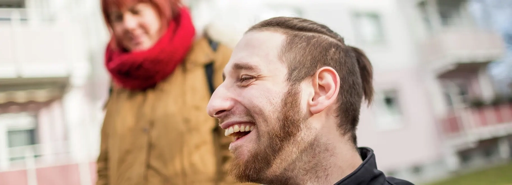 Ein lächelnder junger Mann und eine Frau vor einem Wohngebäude