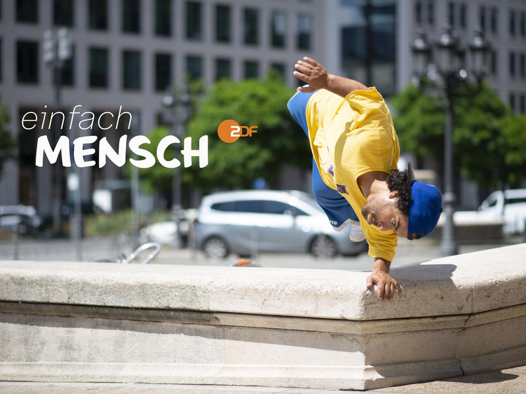 Ein kleinwüchsiger Mann zeigt einen einhändigen Handstand auf einer Mauer mitten in der Stadt. Daneben steht: einfach Mensch und das ZDF-Logo.