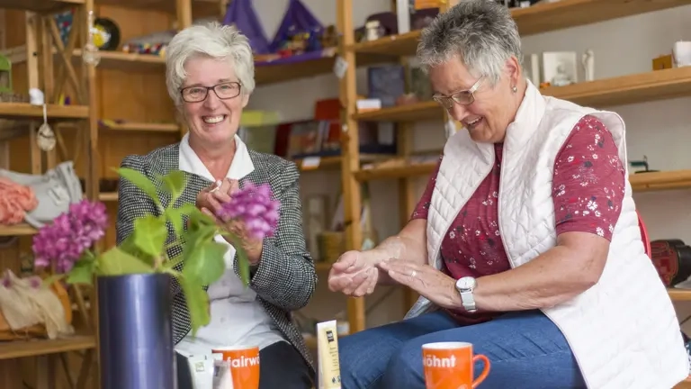 Zwei ältere Frauen sitzen in einem Laden, trinken Kaffee. und lachen